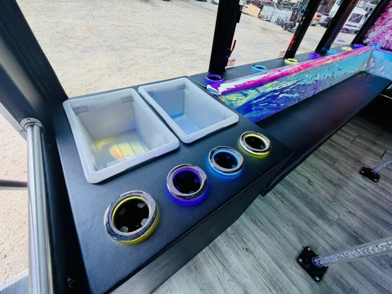 Neon-lit cup holders beside the cooler bins on The Mini Unicorn party bus bar